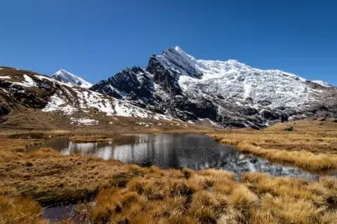 Blick auf eine kleine Lagune und auf schneebedeckte Berge im Hochland der Anden in Peru.