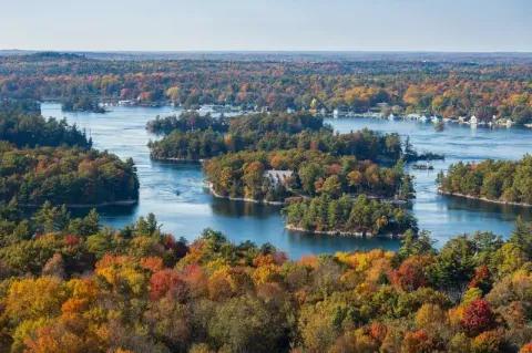 Blick auf eine Flusslandschaft mit kleinen Inseln, auf denen Bäume stehen. Die Bäume sind in Herbstfarben gefärbt.