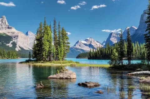 Blick auf einen Gebirgssee, der von felsigen Bergen umgeben ist. Auf dem See sind kleine Inseln zu sehen auf denen vereinzelt Nadelbäume wachsen.