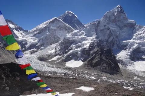 Blick auf spitz zulaufend und mit Schnee bedeckte Gipfel. Vorne im Bild sind buddhistische Gebetsfahnen zu sehen.