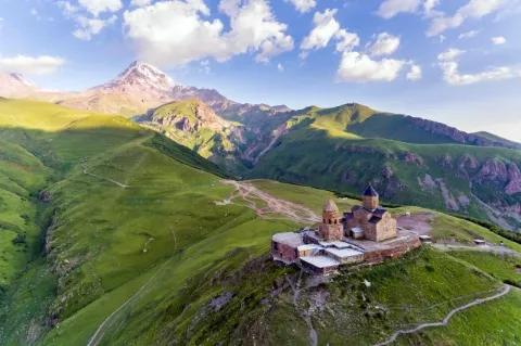 Ein kleiner Kirchenkomplex steht in einer grünen Hügellandschaft.
