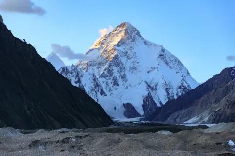 Blick auf den schneebedeckten, spitzigen Gipfel des K2, der von der Sonne beschienen wird.