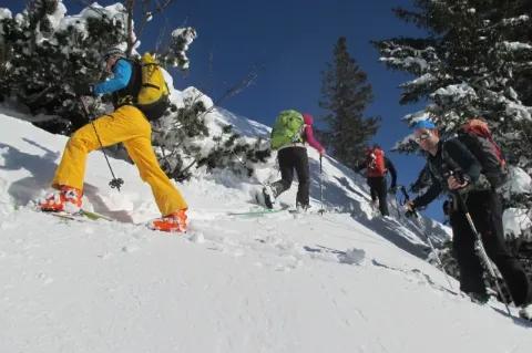 Mehrere Menschen in Winterausrüstung, Schneeschuhen und Skistöcken wandern einen steilen Schneehang hinauf.