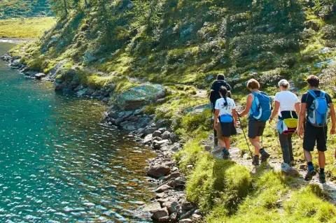 Eine Gruppe von fünf Wanderer geht auf einem schmalen Wanderpfad direkt neben einem türkisblauen See