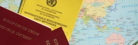 Ein gelber Impfpass und zwei europäische Reisepässe liegen auf einer Landkarte
