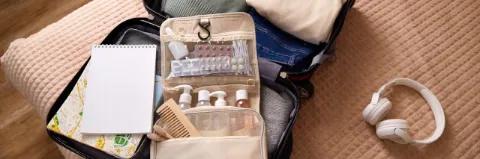 Ein offener Reisekoffer mit Reiseapotheke liegt auf einem Bett
