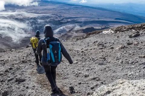 Zwei Wanderer mit Kapuze auf dem Kopf steigen einen steinigen Hang hinunter.