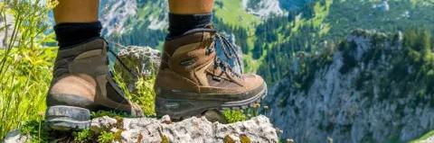 Zwei Füße mit Wanderschuhen sind in Nahaufnahme auf felsigem Untergrund zu sehen.