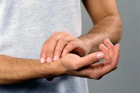 Ein Mensch mit grauen T-Shirt misst mit seiner linken Hand seinen Puls am Handgelenk der rechten Hand.