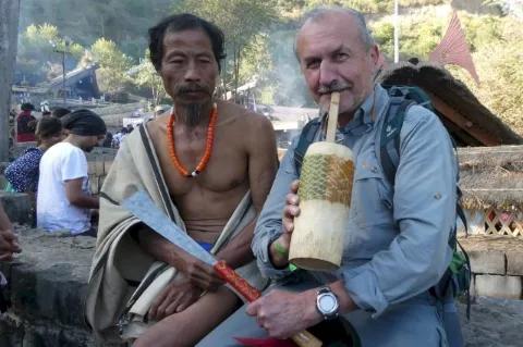 Zwei Männer sitzen auf einer Steinmauer. Der rechte Mann posiert mit einem Trinkbecher aus Holz.