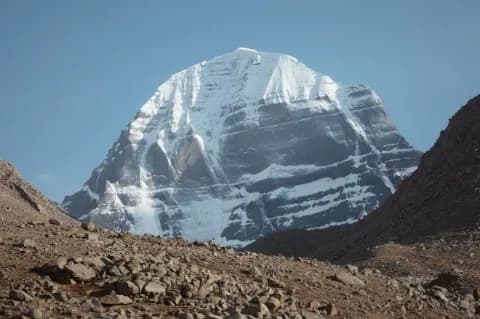 Von einem braunen, gerölligen Berg schaut der Fotograf auf einen schneebedeckten Gipfel.