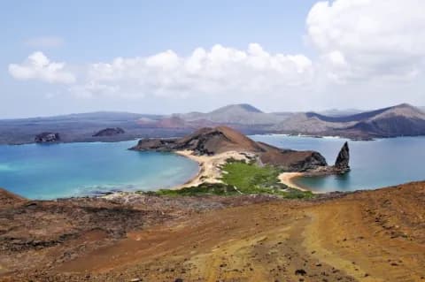 Eine felsige Landschaft. In der Mitte ist blaues Wasser mit einer Landzunge mit zwei Stränden.