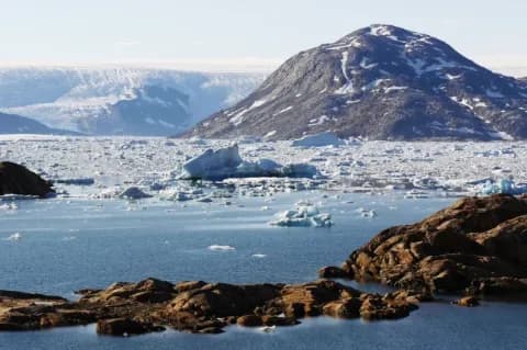 Eisschollen schwimmen in einem Fjord. Ringsum sind Felsen und schneebedeckte Berge.