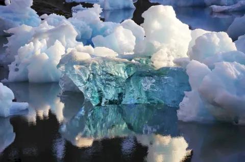 Im Wasser schwimmen kleinere Eisschollen. Eine davon ist komplett vereist und durchsichtig.