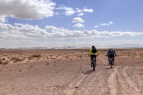 Zwei MTB-Radfahrer, von hinten fotografiert, fahren durch die Wüste auf einem Schotterboden.