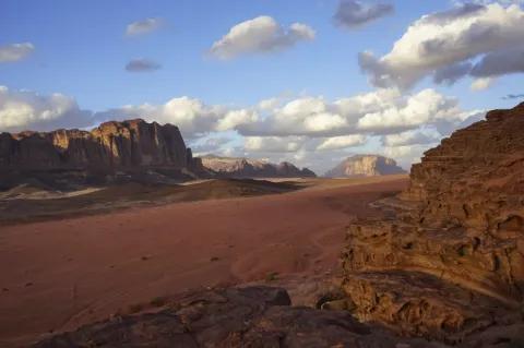 In einer steinigen Wüste sind kantige rötliche Felsen. Die Landschaft ist karg und aus rötlichem Sand.
