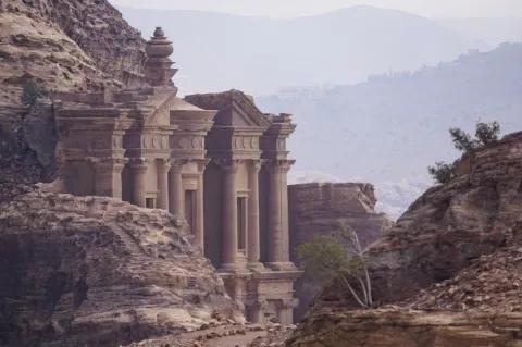 Eine felsige Landschaft. In den Felsen ist ein Tempel aus Stein gebaut. Im Hintergrund sind Berge.