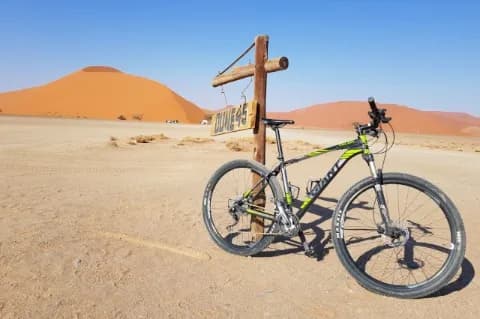 Ein Mountainbike Fahrrad lehnt an einem Schild, auf dem "Dune 45" steht. Dahinter ist eine große Düne.