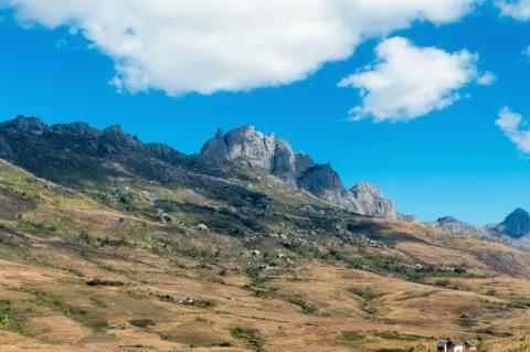 Ein Berg aus orangenem Fels. Er ist teils grün bewachsen. Dahinter ragen noch höhere Berge hervor.
