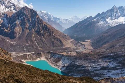 Ein blauer Bergsee in der Mitte. Darum herum sind hohe Gipfel, die teils schneebedeckt sind.