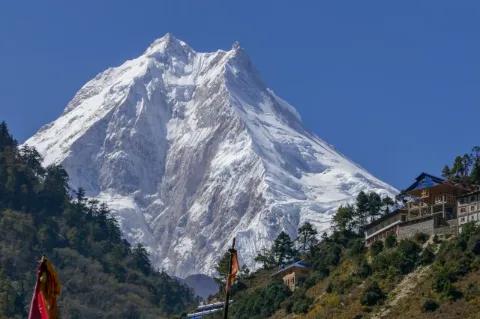 Ein großer schneebedeckter Berg in der Mitte. Rechts und links sind kleinere Berge und Häuser.