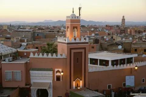 Eine aus Lehmbauten bestehende Stadt. Im Hintergrund sind die Berge und der gelbliche Himmel.