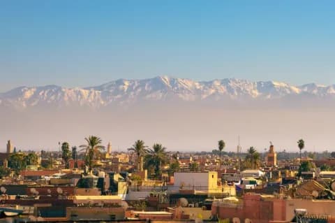 Eine Stadt mit rötlich braunen Gebäuden. Dahinter ist ein hohes, schneebedecktes Gebirge.