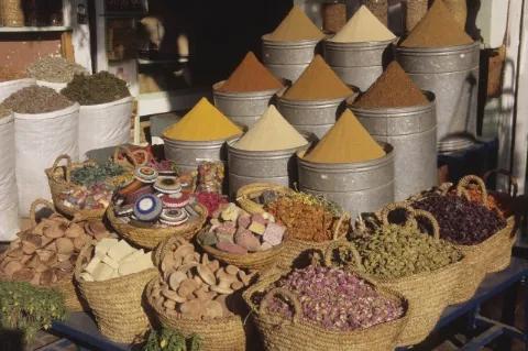 An einem Marktstand sind mehrere große Gefäße mit Gewürzen, Obst und Gemüse.