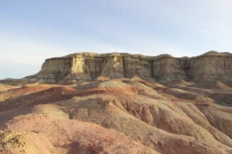 Braun rötliche Hügel, dahinter sind Berge in der gleichen Farbe. Der Himmel ist blau.
