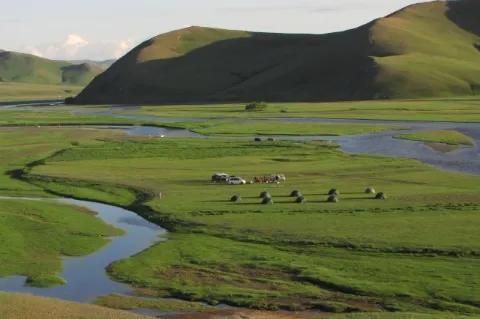 Mehrere grüne Zelte stehen im grünen Tal. Kleine Bäche ziehen durch die Landschaft.