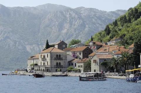 An der Küste befindet sich eine kleine Stadt. Es fahren Boote. Im Hintergrund sind die Berge.
