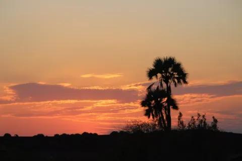 Die untergehende Sonne hat den Himmel rötlich gefärbt. Die Umrisse der Landschaft erscheinen schwarz.