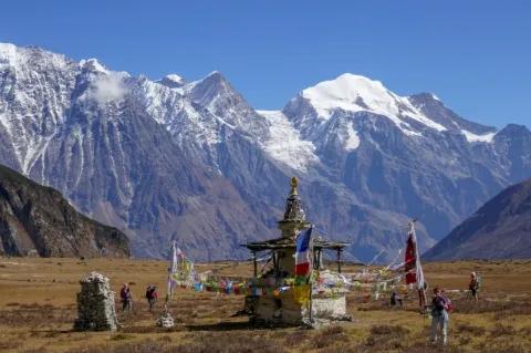 Mehrere Wanderer stehen um einen buddhistischen Schrein. Im Hintergrund sind schneebedeckte Berge.