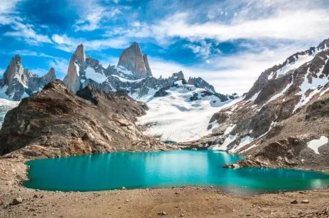 Eine blaue Lagune zwischen Felsen und hohen schneebedeckten Bergen.