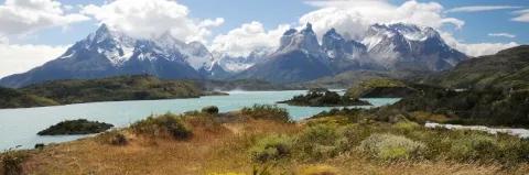 Ein blauer See. Im Hintergrund sind hohe schneebedeckte Berge, in denen die Wolken hängen.