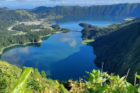 Eine Lagune umgeben von grün bewachsenen Hügeln. Auf der linken Seite ist ein kleines Dorf.