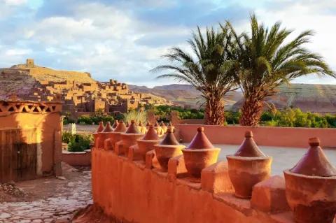 Eine Stadt in der Wüste. Im Vordergrund ist eine Stadtmauer und zwei Palmen.