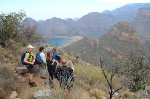 Sechs Wanderer stehen am Hang und genießen die Aussicht ins Tal und zum See.