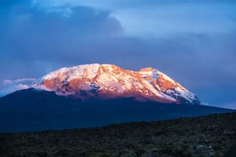 Der Gipfel eines schneebedeckten Berges wird von der aufgehenden Sonne angestrahlt.