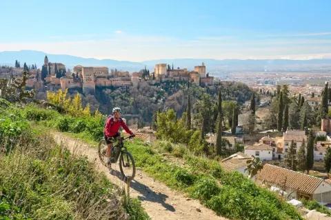 Eine Frau radelt mit ihrem Elektro-Mountainbike in Granada unterhalb des Weltkulturerbes Alhambra