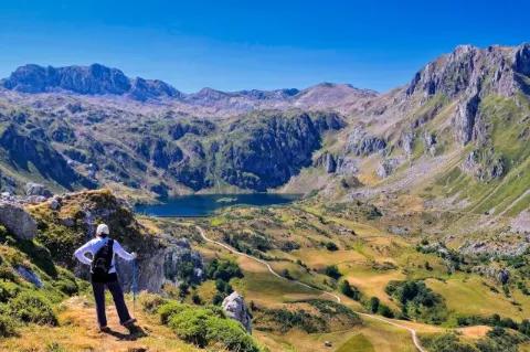Eine Frau steht auf einem kleinen Absatz und blickt auf die hügelige und felsige Landschaft unter sich.