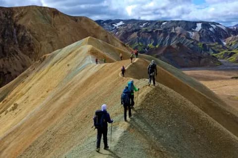 Trekkinggruppe läuft bei bewölktem Himmel über die Berge auf einem schmalen Grat