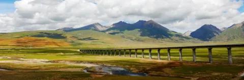 In einer grünen Landschaft mit Bergen und kleinen Wasserlöchern ist eine lange Zugbrücke.