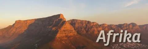 Unten rechts am Bild steht "Afrika". Dahinter ist ein Bergmassiv , das rot scheint. Die Sonne geht unter.