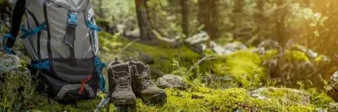 Wanderrucksack und Wanderschuhe stehen im Wald bei leichtem Sonnenschein