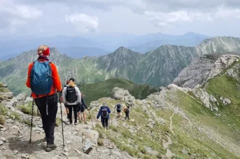 Sechs Personen mit Wanderstöcken laufen hintereinander über einen Grat bei bewölktem Himmel
