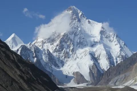 Frontaler Blick auf einen imposanten, schneebedeckten Berggipfel in einer felsigen Umgebung.