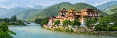 Klosteranlage mit roten Dächern steht an einem Fluss umgeben von grüner Landschaft