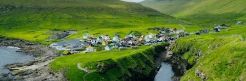 Luftaufnahme von Dorf an der Küste umringt von grünen Wiesen und grünen Berghängen