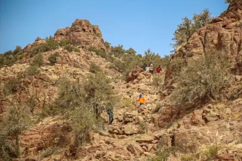 Vereinzelte Wanderer steigen eine steile, rotbraune Felswand hinunter.